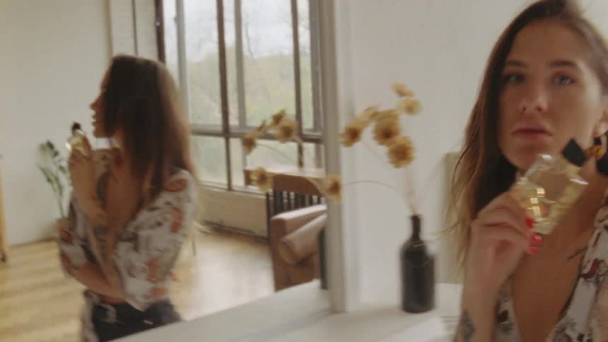 Woman stands looking in mirror then displays perfume bottle