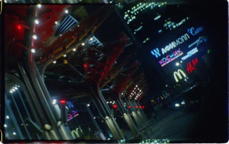 An urban area is visible at night with several illuminated signs seen ahead