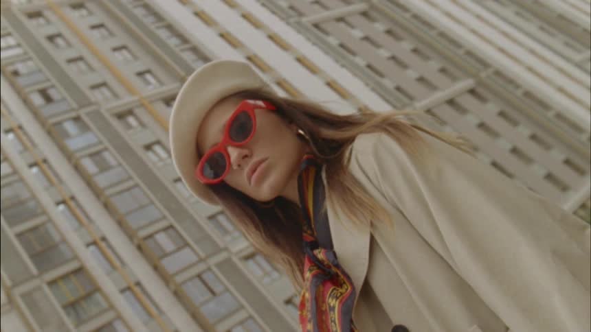 A woman wearing red sunglasses stands in front of a tall apartment building