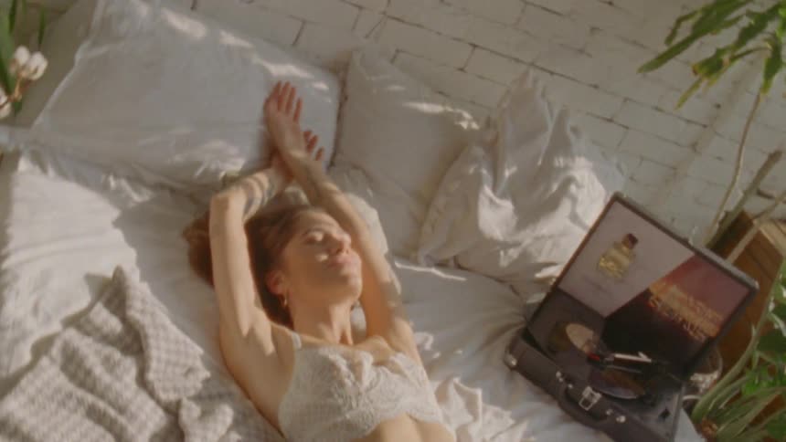 A woman lays in a bed wearing lingerie and a record player beside her