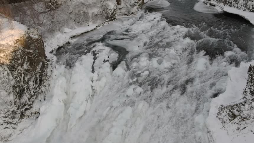 A waterfall partially frozen by ice surrounded by rocky cliffs and trees