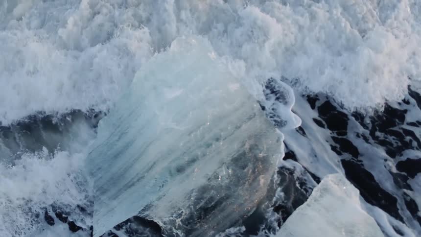 A large piece of ice floats in the ocean with waves crashing against it