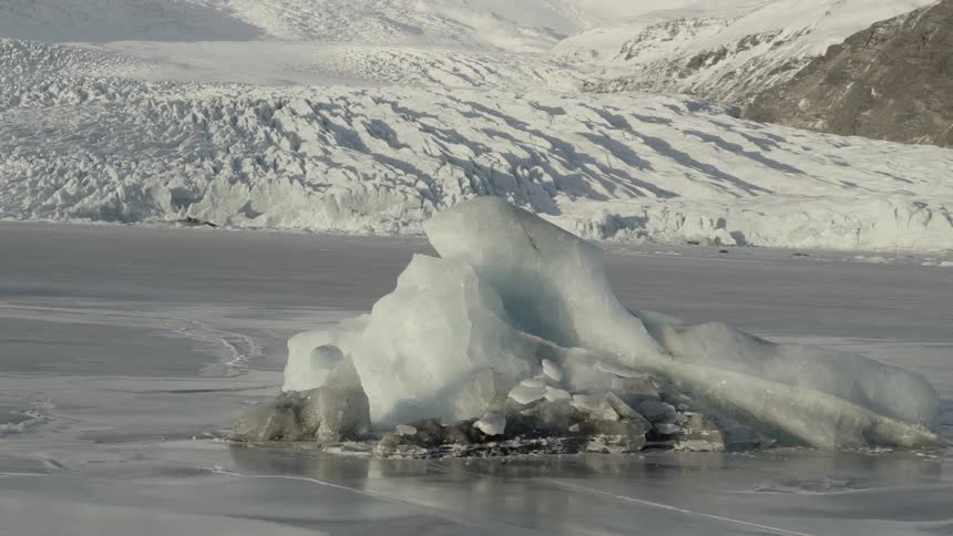A chunk of ice sits on a frozen body of water