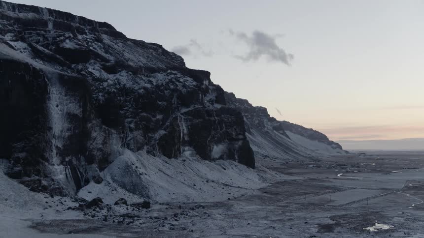 Flat land is covered in snow and overshadowed by a mountain as the sun dawns