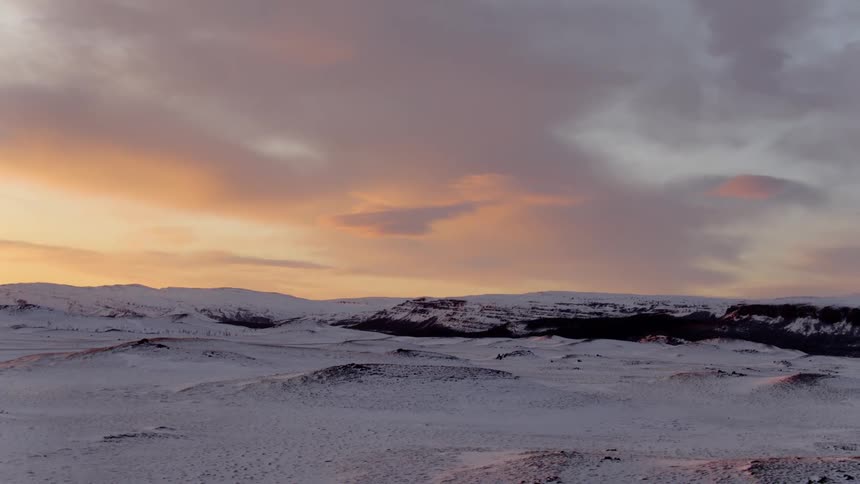 A rocky and mountainous tundra is covered in a layer of snow under a cloudy sky