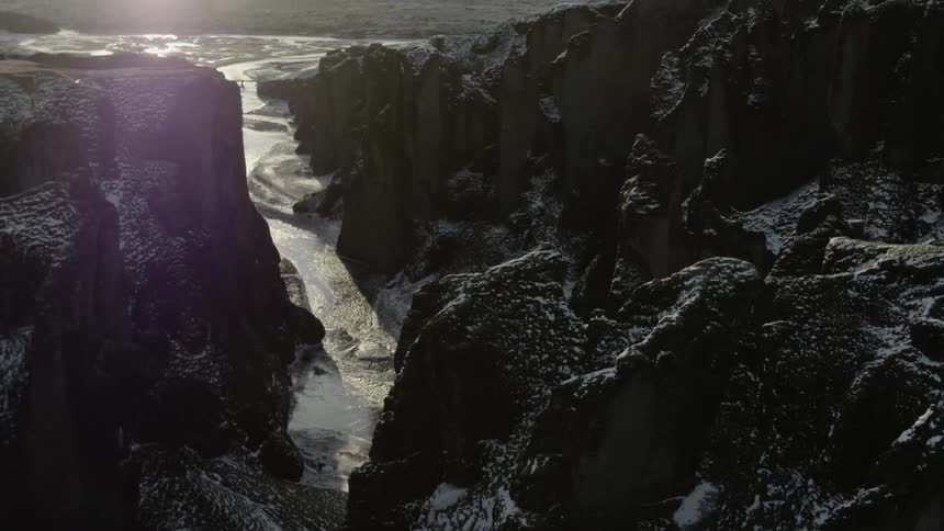 A range of dark mountains are dusted with snow as a river that is can be seen flowing through a deep canyon cut through the mountain range