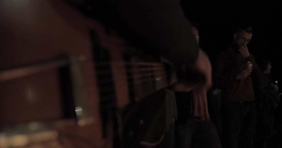 A man holding an electric guitar strums away on it while standing around several other people in a darkened area