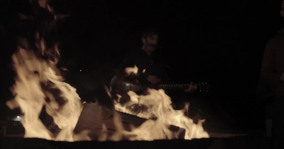Man plays guitar next to bonfire at night