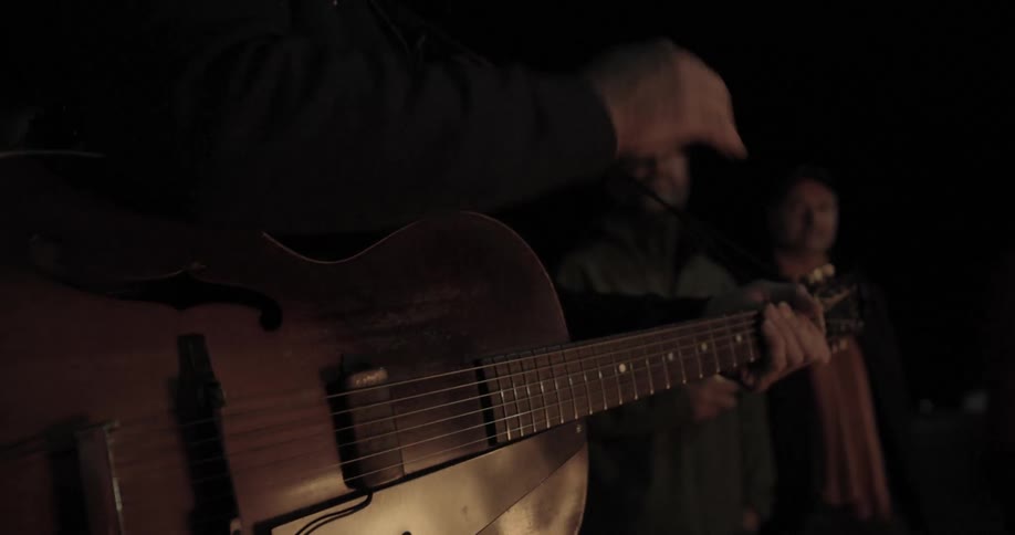 People are gathered outside as someone plays guitar at night