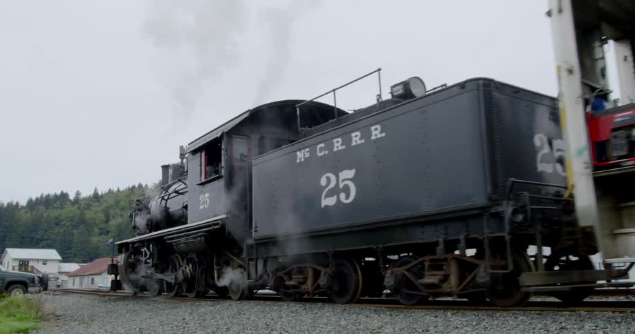 A steam locomotive pulls a train car past a stopped pickup