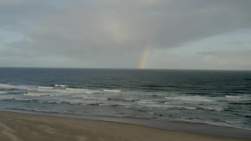 A rainbow peaks through the clouds and falls to the ocean water