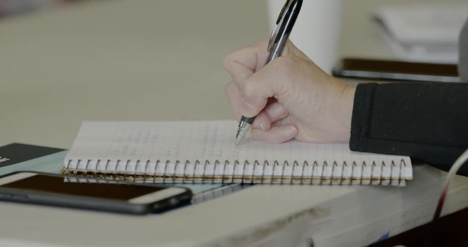 Person writing notes in a spiral bound notebook with a black pen