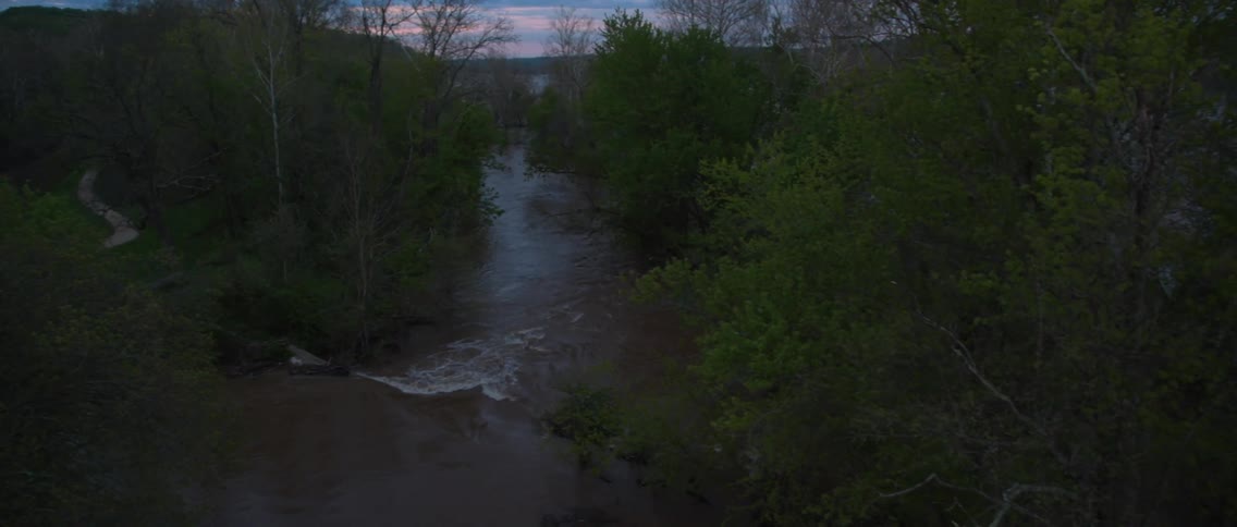 A stream is seen in the middle of a forest at sunset