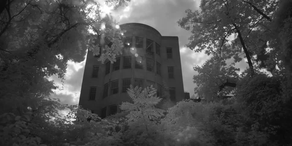 The sun is shining behind a large building behind a forest