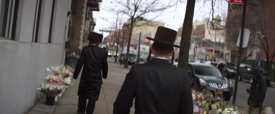 Hasidic jews walking down an urban street and a flower shop