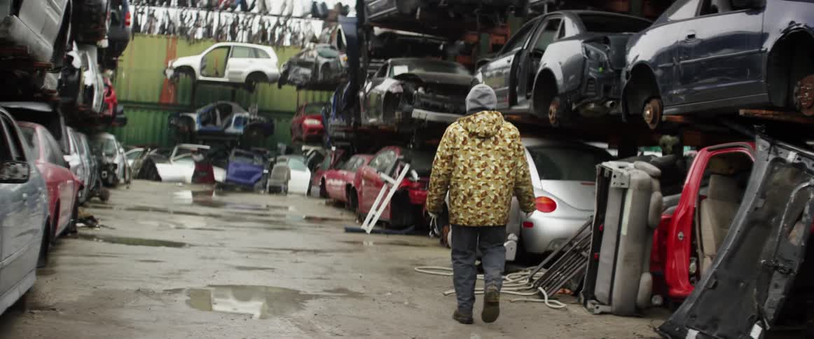 A person in a heavy coat walks through an auto wrecking yard