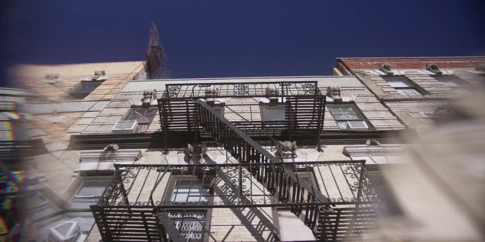 Fire escape stairs attached to an older building as the camera angle rises up toward the roof