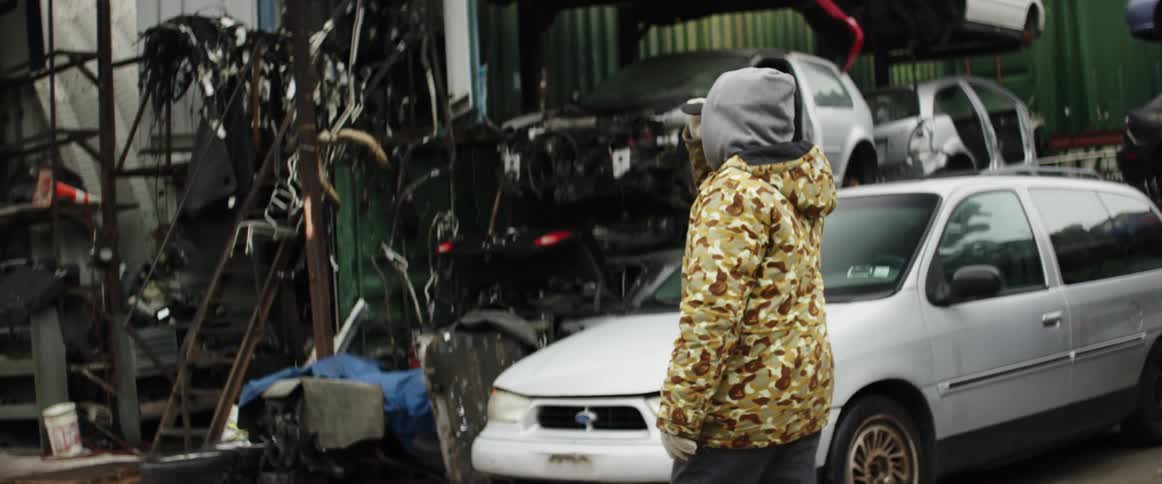 A man walks by cars in a junkyard