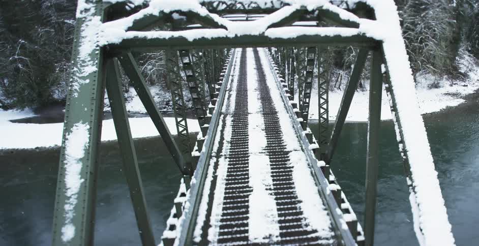Snow falls around a rural bridge