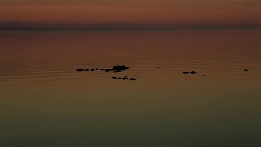 A large body of water has rocks floating in it at sunset