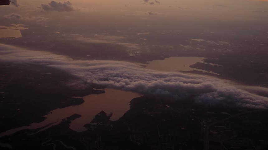 A handful of fluffy clouds float in the sky and below a large lake can be seen that is bordered by a city