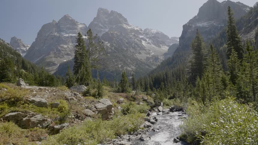 A small brook running down the foothills of large mountains in the distance