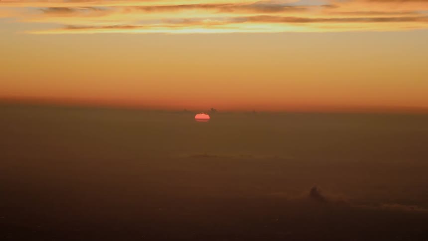 In the horizon the sun hangs low in the sky and casts an orange glow from behind a think layer of clouds