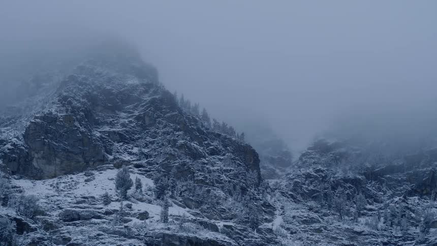 A thick layer of cloudy fog covers the top of a rocky and snow covered mountain in the midst of winter