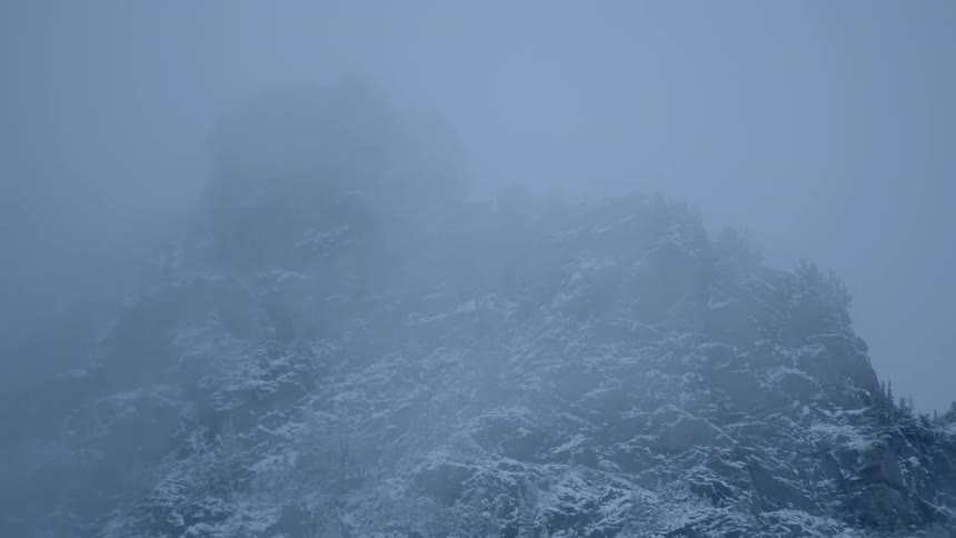 A layer of clouds passes in front of the snow covered summit of a mountain in the midst of winter