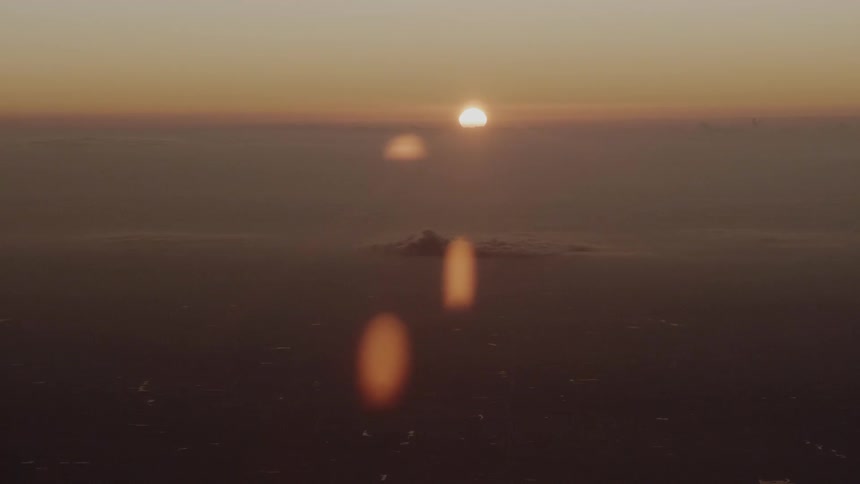 A the summit of a large mountain just barely protrudes through a thick layer of clouds above which the sun is low in the sky