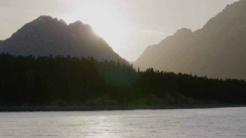 A lake and hills with the sun peaking above
