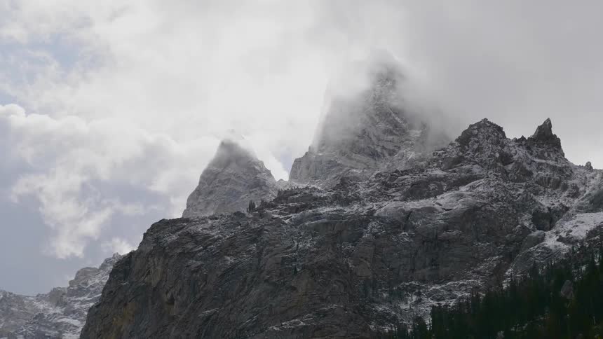 Clouds at the peak of a snow covered mountaintop