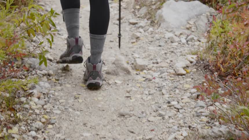 A woman hikes down a rocky path with vegetation on the sides