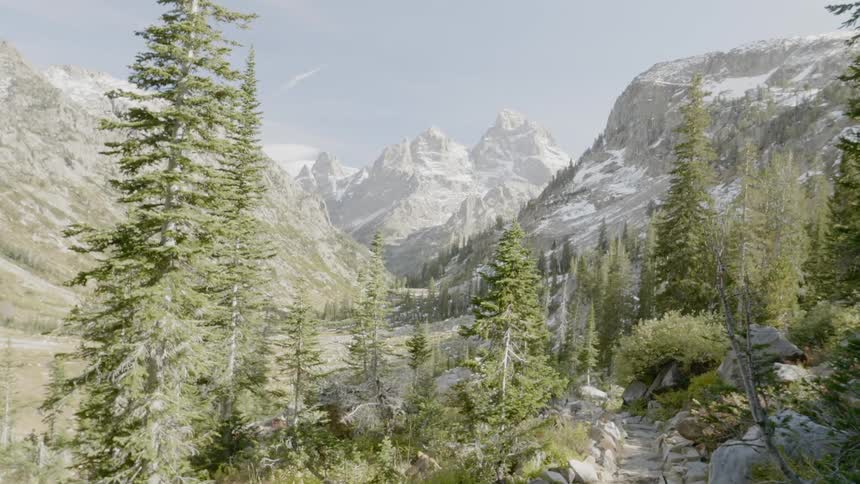 Evergreen trees stand at the base of rocky mountain slopes dusted with snow