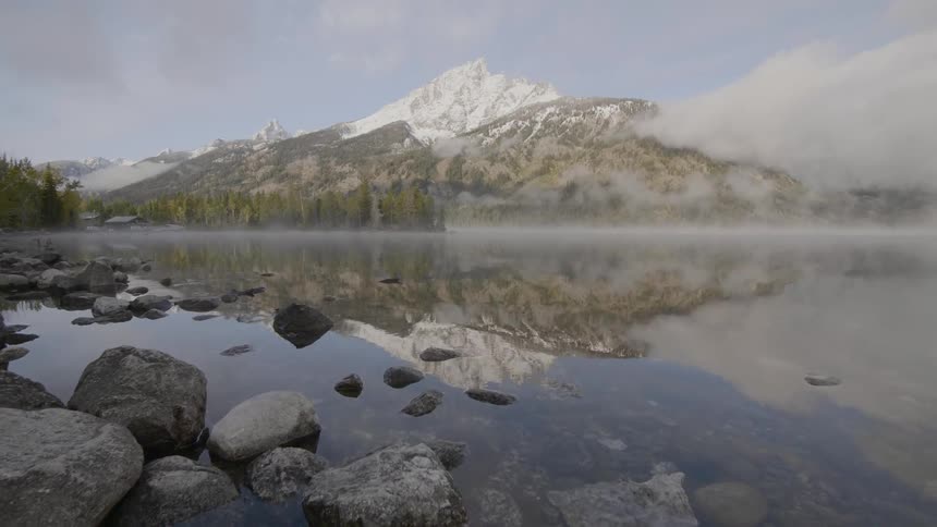 A calm body of water reflecting a snow capped mountain shrouded in mist