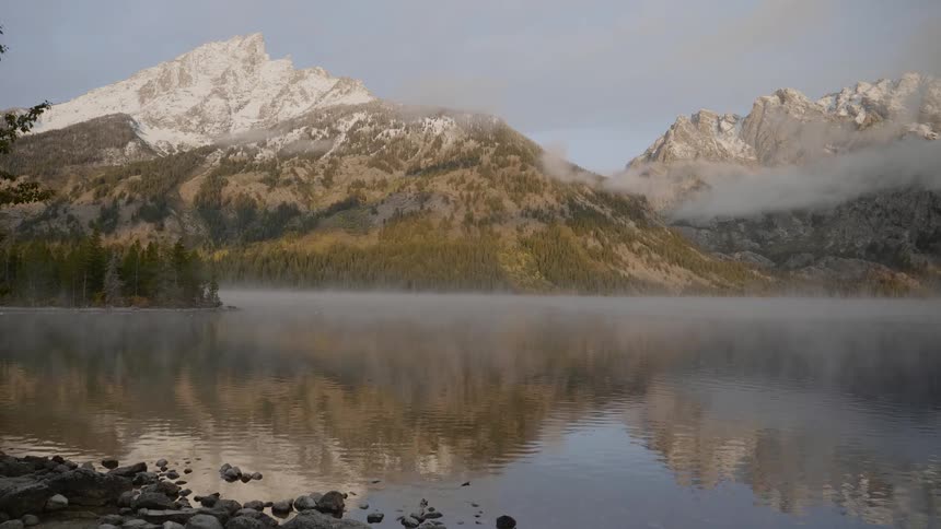 The reflection of range of mountains on the surface of a lake can be seen on a foggy day