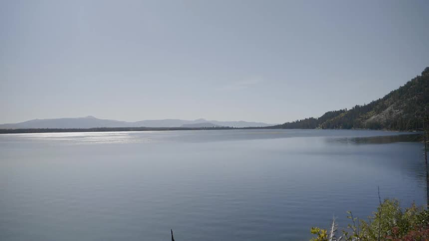 The surface of a blue lake ripples as it reaches toward shore