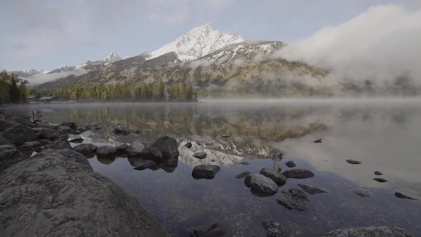 The peak of a towering mountain top is covered in snow and its reflection can be seen on the surface of the nearby lake