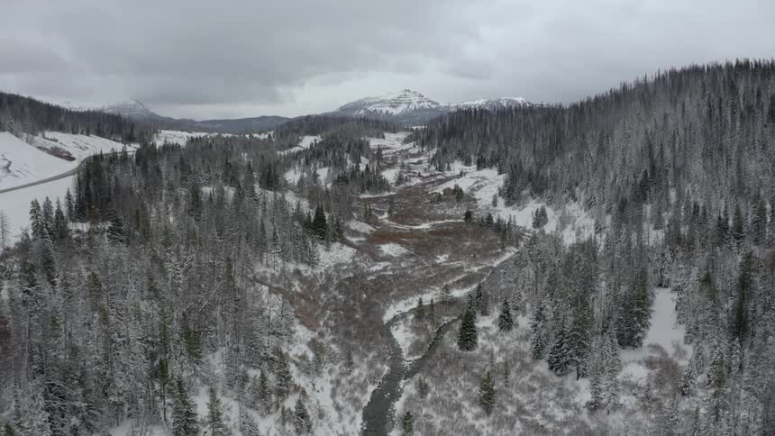A narrow river in a valley between two snowy hills covered in trees
