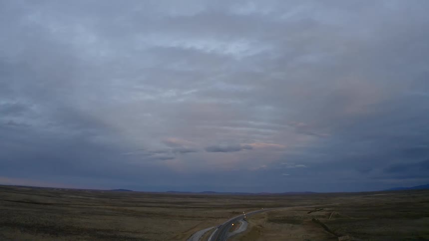 Aerial view of road through grassland plains under a cloudy sky