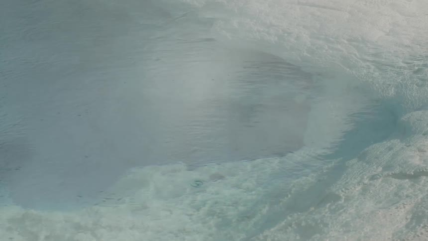Steam floats over the surface of a clear hot spring surrounded by rock
