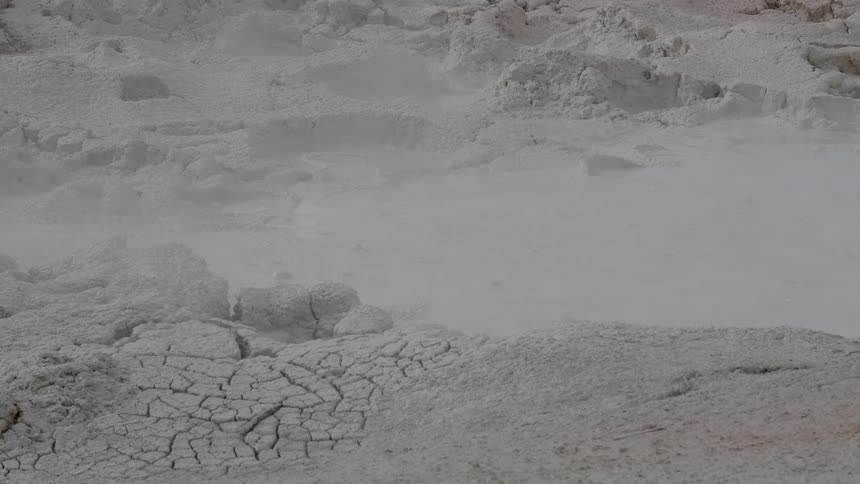 Steam rises from a small pool of bubbling and boiling water in a natural hot spring in the ground