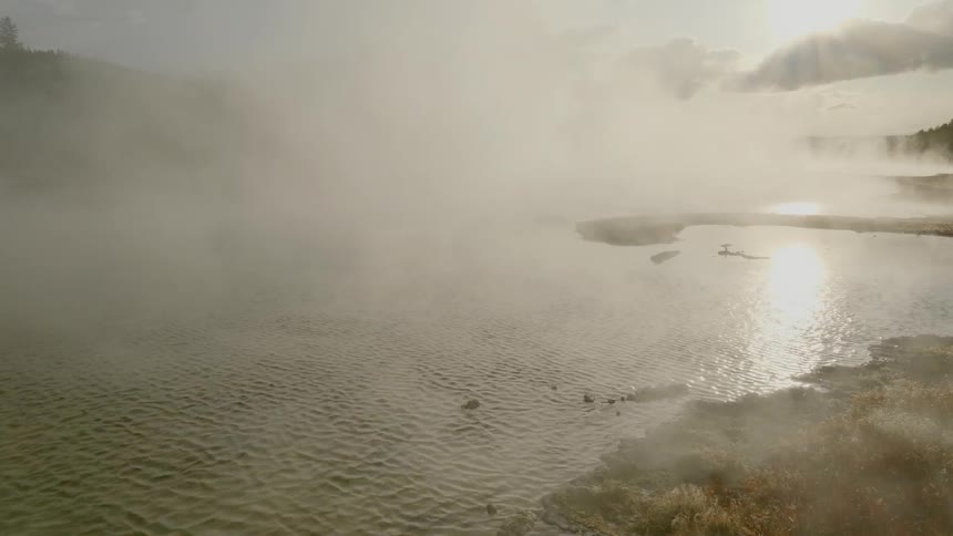 Steam rises and from the surface of a natural hot spring and is away by the wind on a sunny day