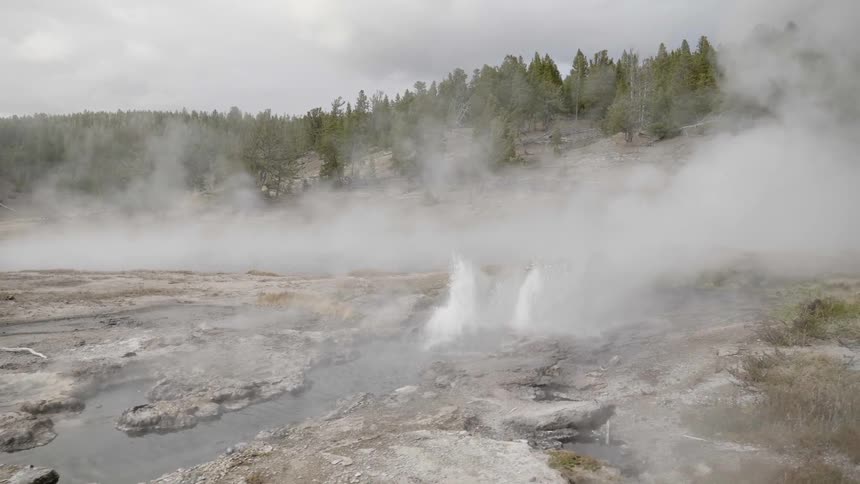Water shoots up and steam rises from hot springs and geysers on a winter day
