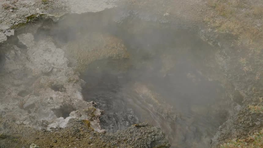 Steam rises from a hot spring bubbling in a rocky surface