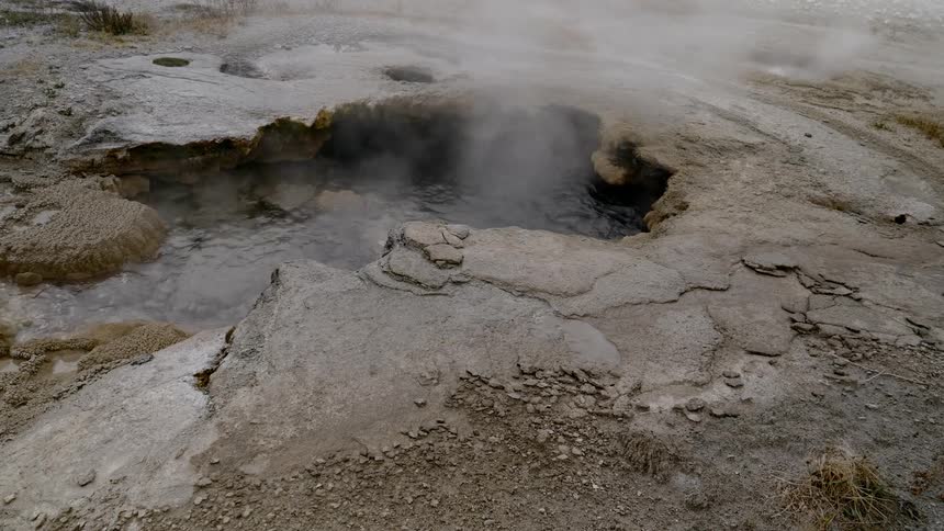 A geyser with water bubbling in it and steam rising from it