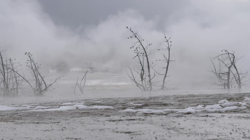 A hot spring at wintertime producing steam with a road and cars in the background