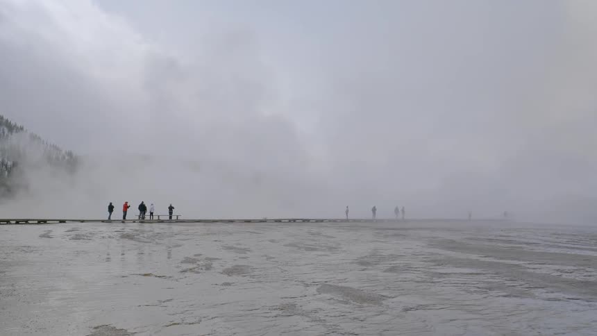 People stand on a wooden bridge and watch steam geysers fire off