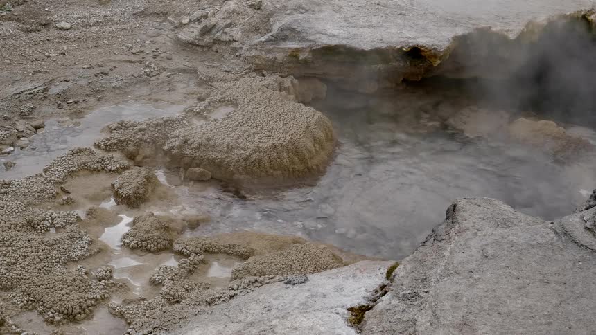 Water can be seen bubbling and boiling within a natural hot spring that is surrounded by rocks covered in crystalline mineral deposits