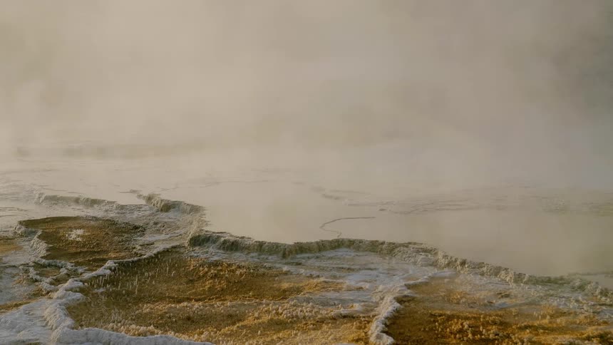Mist billows above a body of water that is surrounded by rocks